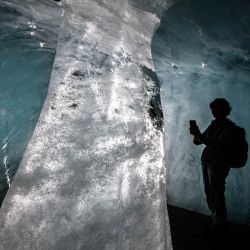 Esta fotografía muestra a un turista tomando imágenes de una columna de hielo en el interior de una cueva —ahora mucho más pequeña— del glaciar del Ródano, en los Alpes suizos, cerca de Gletsch. Tras el calor extremo de junio y julio, el glaciar del Ródano ha perdido más de cuatro metros de hielo en un solo mes, según el glaciólogo Matthias Huss, director de la Red Suiza de Monitoreo de Glaciares (GLAMOS), citado por la agencia de noticias suiza Keystone-SDA. El retroceso del glaciar, que promedia unos 10 centímetros diarios, ha generado preocupación de que 2026 pueda igualar la pérdida de hielo récord registrada en 2022. | Foto:FABRICE COFFRINI / AFP
