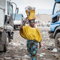Ngendakumana Aline, de 48 años, lleva sobre la cabeza un balde amarillo lleno de fragmentos de carbón y materiales reciclables mientras pasa junto a camiones de basura en el vertedero de Mubone, en el distrito de Buterere, Buyumbura. En el vertedero de Mubone —el principal basurero que da servicio a Buyumbura, la capital comercial de Burundi—, cientos de mujeres pasan sus días buscando fragmentos de carbón y materiales reciclables para venderlos en los mercados locales. Muchas de ellas son el único sustento de sus familias y ganan alrededor de 2000 francos burundeses (aproximadamente 0,70 dólares) al día; una labor que realizan en un contexto marcado por una grave inflación y una escasez de combustible a nivel nacional, factores que han impulsado la demanda de fuentes de energía doméstica más económicas. | Foto:Herve Shabani / AFP