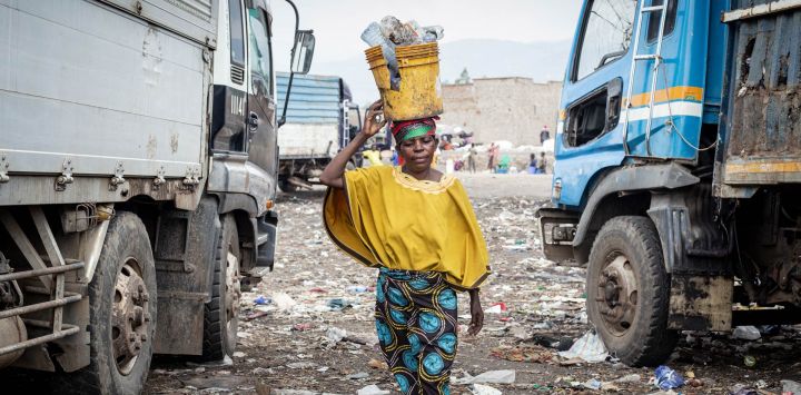 Ngendakumana Aline, de 48 años, lleva sobre la cabeza un balde amarillo lleno de fragmentos de carbón y materiales reciclables mientras pasa junto a camiones de basura en el vertedero de Mubone, en el distrito de Buterere, Buyumbura. En el vertedero de Mubone —el principal basurero que da servicio a Buyumbura, la capital comercial de Burundi—, cientos de mujeres pasan sus días buscando fragmentos de carbón y materiales reciclables para venderlos en los mercados locales. Muchas de ellas son el único sustento de sus familias y ganan alrededor de 2000 francos burundeses (aproximadamente 0,70 dólares) al día; una labor que realizan en un contexto marcado por una grave inflación y una escasez de combustible a nivel nacional, factores que han impulsado la demanda de fuentes de energía doméstica más económicas.