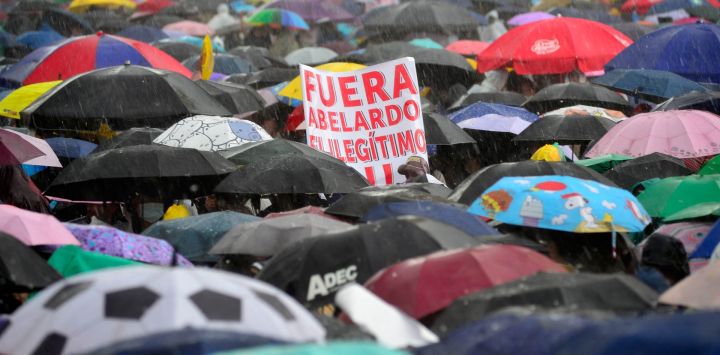 Se observa una pancarta con la leyenda "Fuera Abelardo, ilegítimo" mientras los manifestantes se resguardan bajo paraguas durante una protesta contra el gobierno del presidente colombiano Abelardo de la Espriella en Bogotá, en el marco de una jornada nacional de manifestaciones convocada por sindicatos, organizaciones de maestros, grupos estudiantiles y sectores de la oposición.