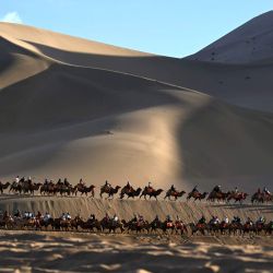 Imagen de turistas montando camellos en el área escénica de la Montaña Mingsha y el Manantial de la Luna Creciente, en Dunhuang, en la provincia de Gansu, en el noroeste de China. En promedio diario, el número de viajes dentro del territorio nacional aumentó un 6,3 por ciento en comparación con los ocho días de la temporada vacacional con motivo del Día Nacional y el Festival del Medio Otoño de 2025, mientras que el gasto en turismo creció un 4,3 por ciento, según el Ministerio de Cultura y Turismo. | Foto:Xinhua/Zhang Xiaoliang