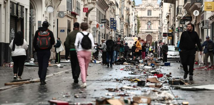 Unos peatones caminan por una calle cubierta de escombros, un día después de las protestas a nivel nacional contra el "alto costo de la vida", en Marsella. El primer ministro de Francia informó que 1200 personas fueron detenidas durante las protestas en todo el país y que 150 agentes de policía resultaron heridos en los enfrentamientos entre las fuerzas de seguridad y los manifestantes. Saqueos masivos e incendios múltiples se extendieron por Francia, a medida que las marchas nacionales contra la inflación desbocada degeneraban en una violencia callejera de extrema intensidad.