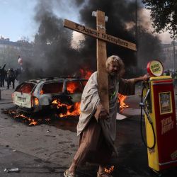 Un manifestante sostiene una cruz con la inscripción "el amor triunfará" junto a un surtidor de gasolina, durante una protesta contra el alto costo de la vida en la plaza de la República, en París. La movilización forma parte de un llamamiento a nivel nacional que ha reunido a diversos grupos que expresan su descontento: antiguos "chalecos amarillos", estudiantes de secundaria y universitarios, activistas climáticos e incluso agricultores. | Foto:Kiran Ridley / AFP
