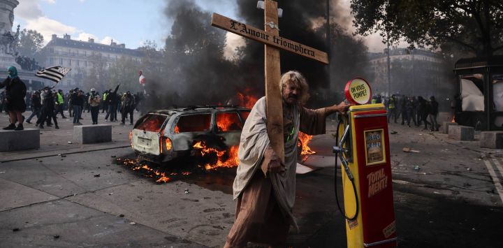Un manifestante sostiene una cruz con la inscripción "el amor triunfará" junto a un surtidor de gasolina, durante una protesta contra el alto costo de la vida en la plaza de la República, en París. La movilización forma parte de un llamamiento a nivel nacional que ha reunido a diversos grupos que expresan su descontento: antiguos "chalecos amarillos", estudiantes de secundaria y universitarios, activistas climáticos e incluso agricultores.