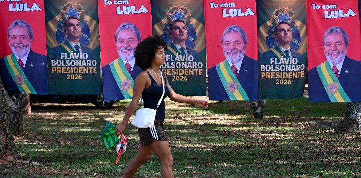 Una mujer pasa junto a banderas y toallas —a la venta en una calle de Brasilia — que exhiben las imágenes del presidente de Brasil y candidato presidencial, Luiz Inácio Lula da Silva, y del senador de derecha y también candidato presidencial, Flávio Bolsonaro. Lula da Silva y Bolsonaro durante la segunda vuelta electoral.