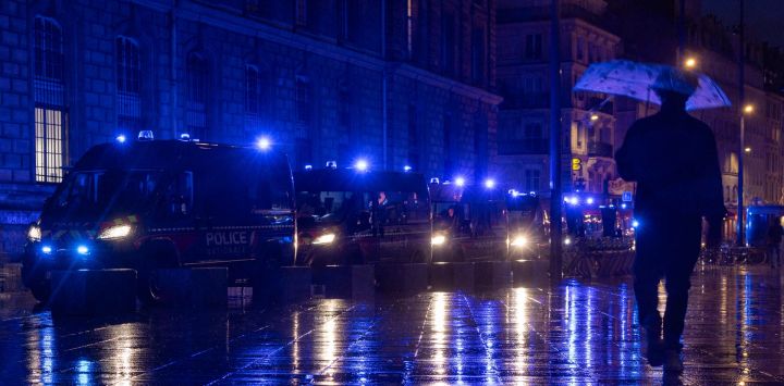 Un peatón con paraguas pasa junto a vehículos policiales estacionados cerca de la plaza de la República durante una manifestación a favor del poder adquisitivo, la protección de los servicios públicos y la justicia fiscal y social, celebrada en París. La protesta formó parte de una convocatoria de movilización a escala nacional que reunió a antiguos miembros del movimiento de los "chalecos amarillos", sindicatos, así como a estudiantes de secundaria y universitarios.