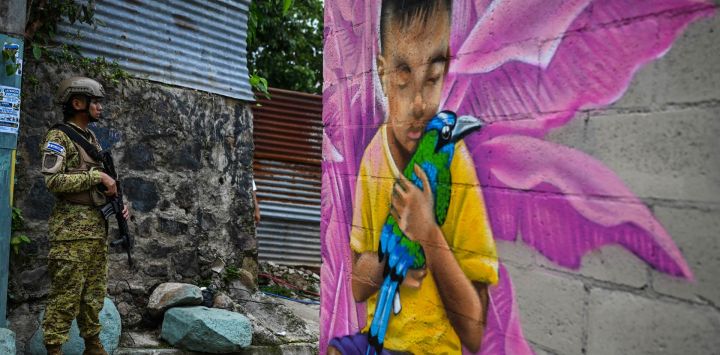 Un soldado salvadoreño monta guardia en un pasaje estrecho de la comunidad 10 de Octubre, frente a un mural pintado por el artista Carlos Clímaco, en San Marcos, El Salvador. El proyecto artístico busca transformar la identidad de una comunidad históricamente afectada por la violencia de las pandillas.